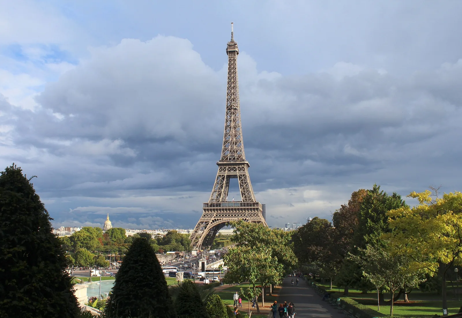 Tháp Eiffel vươn cao giữa khu vườn xanh ở Paris dưới bầu trời nhiều mây kịch tính.
