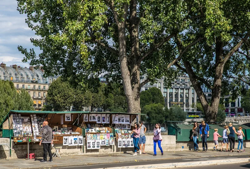 Những quầy sách bouquiniste bên bờ sông rợp bóng cây với người dạo bộ qua lại ở Paris.