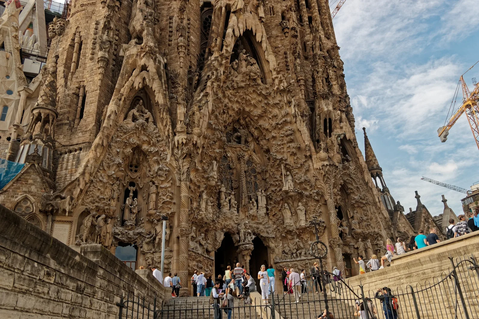 Du khách tụ tập dưới mặt tiền Giáng Sinh chạm khắc tinh xảo của nhà thờ Sagrada Família ở Barcelona, phía sau có cần cẩu.