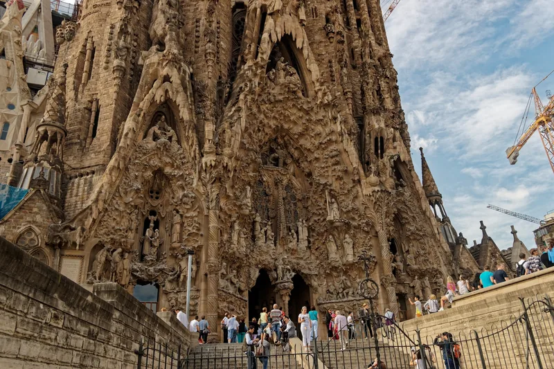 Du khách tụ tập dưới mặt tiền Giáng Sinh chạm khắc tinh xảo của nhà thờ Sagrada Família ở Barcelona, phía sau có cần cẩu.