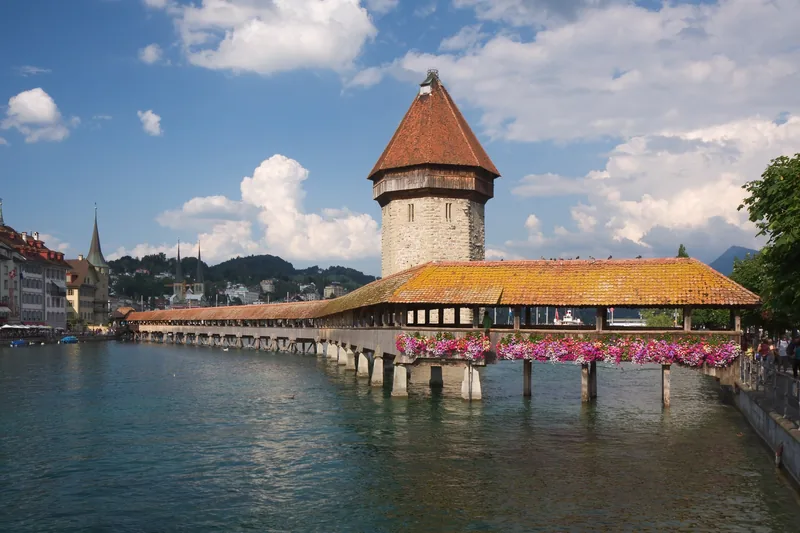 Cầu gỗ Chapel Bridge cùng tháp nước bát giác bắc qua sông ở Lucerne dưới bầu trời xanh.