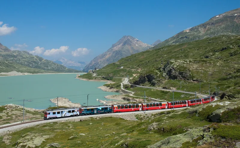 Tàu Bernina Express màu đỏ chạy dọc hồ nước xanh ngọc giữa những dãy núi ở Thụy Sĩ.