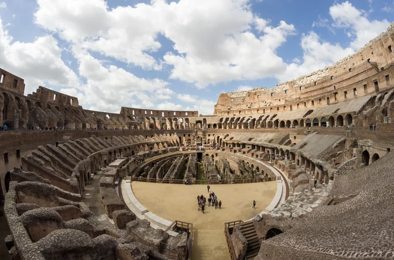 Khán đài và đấu trường bên trong đấu trường Colosseum ở Rome dưới bầu trời nhiều mây.