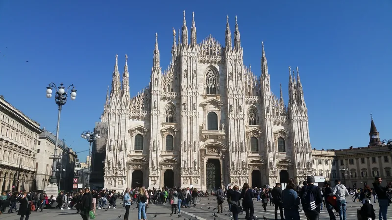 Mặt tiền kiểu Gothic và các tháp nhọn của Nhà thờ Milan vươn cao trên quảng trường đông người dưới trời xanh.