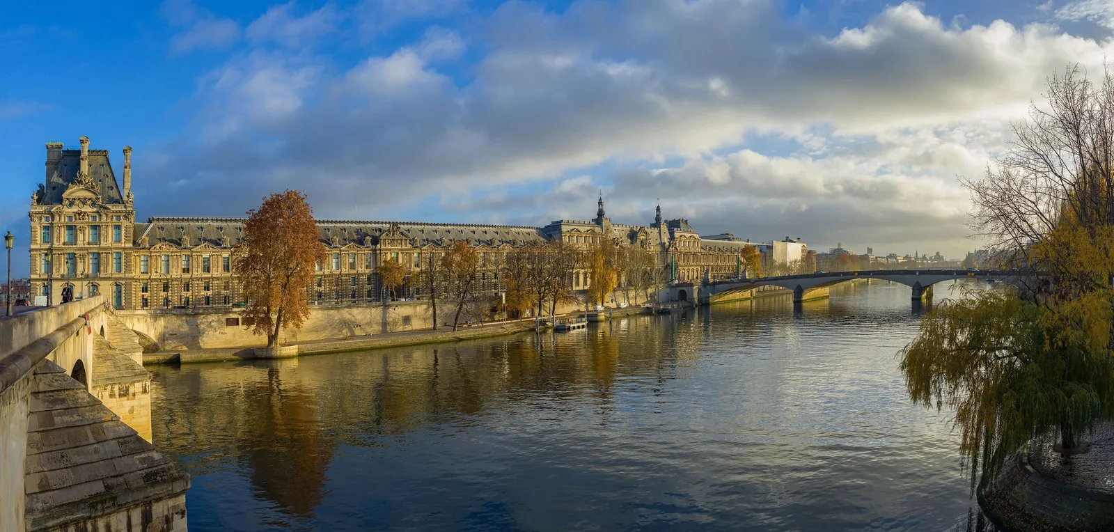 Sông Seine chảy ngang mặt tiền bảo tàng Louvre dưới bầu trời nhiều mây ở Paris.