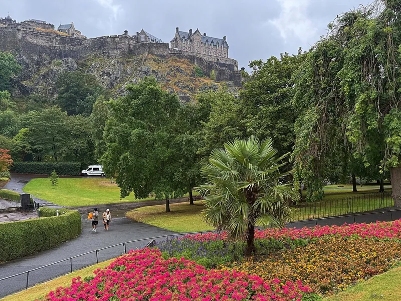 Lâu đài Edinburgh sừng sững trên đồi đá, nhìn xuống vườn hoa rực rỡ và cây xanh của Princes Street Gardens.