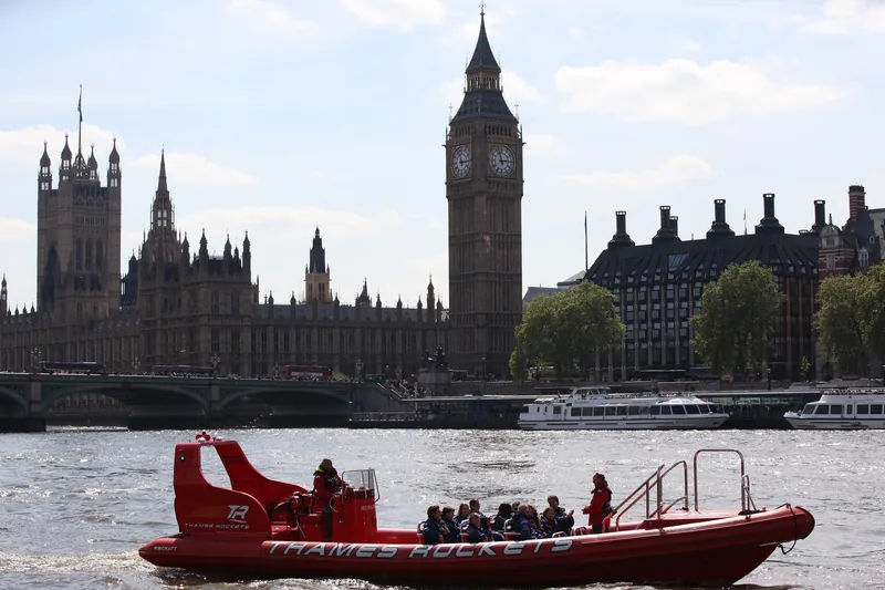 Thuyền cao tốc màu đỏ chở hành khách trên sông Thames với tháp Big Ben và tòa nhà Quốc hội phía sau, London.