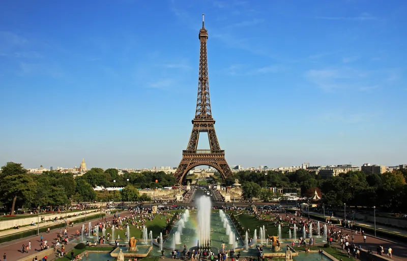Tháp Eiffel vươn cao phía trên vườn hoa và đài phun nước Trocadéro dưới bầu trời xanh ở Paris.
