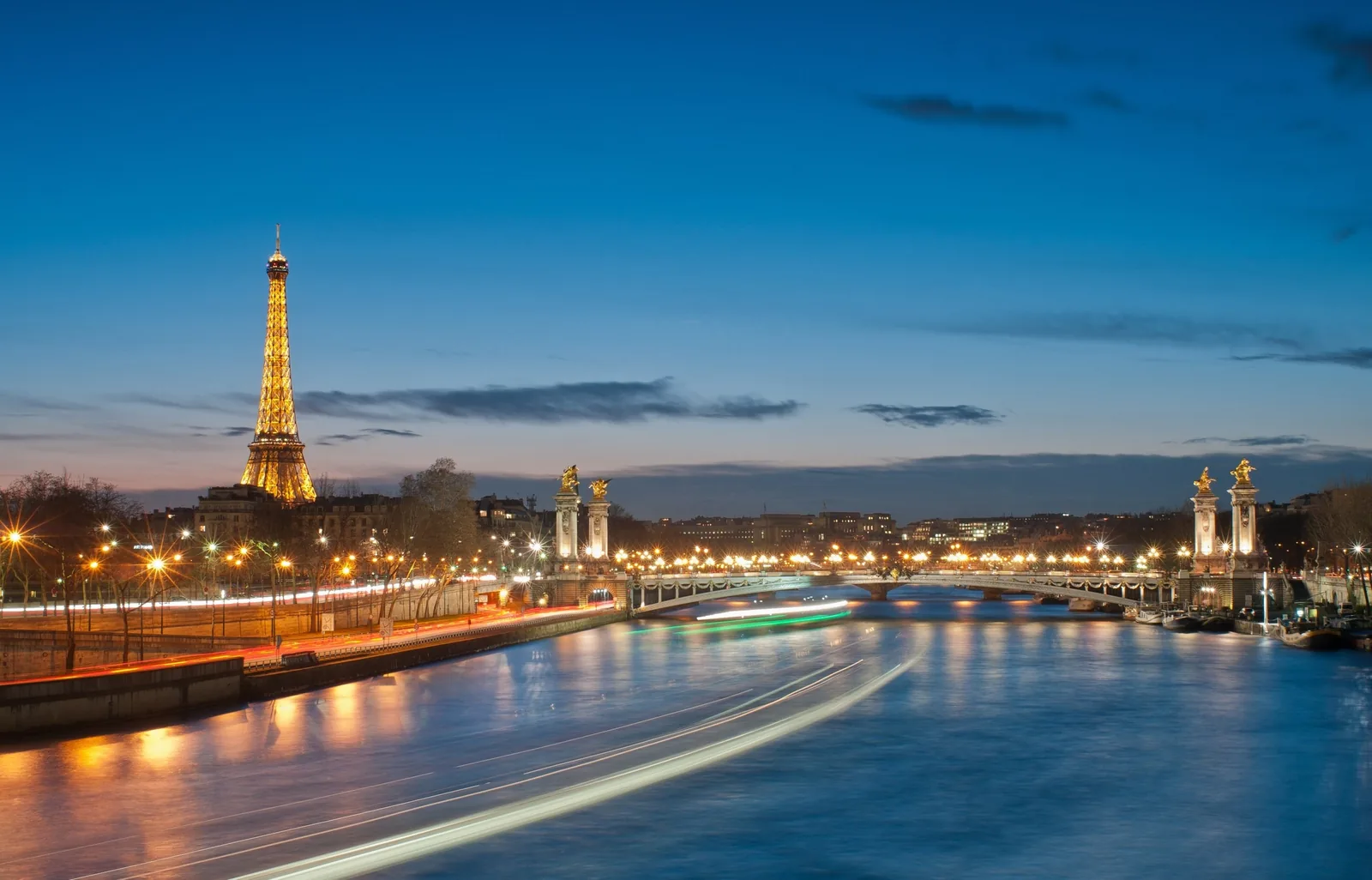 Tháp Eiffel và cầu Alexandre III rực sáng bên dòng sông Seine lúc hoàng hôn ở Paris.