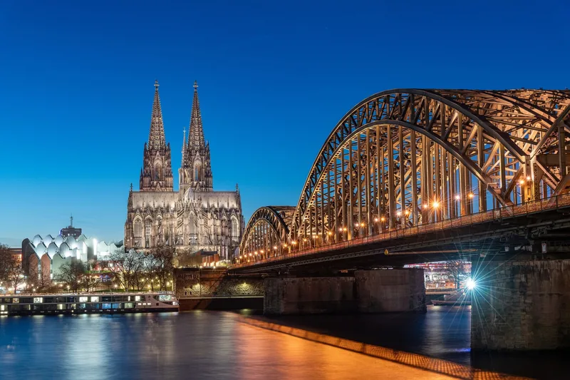 Nhà thờ lớn Cologne và cầu Hohenzollern rực sáng lúc hoàng hôn bên sông Rhine.