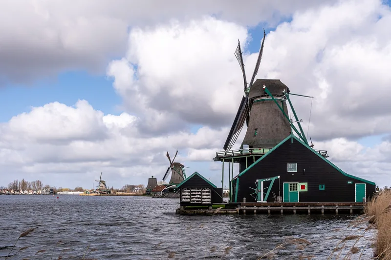 Những cối xay gió truyền thống nằm bên bờ nước tại Zaanse Schans, Hà Lan dưới bầu trời nhiều mây.
