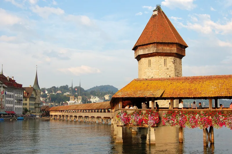 Cây cầu gỗ có mái che và tháp đá cổ với các giỏ hoa rực rỡ bắc qua sông ở Lucerne.