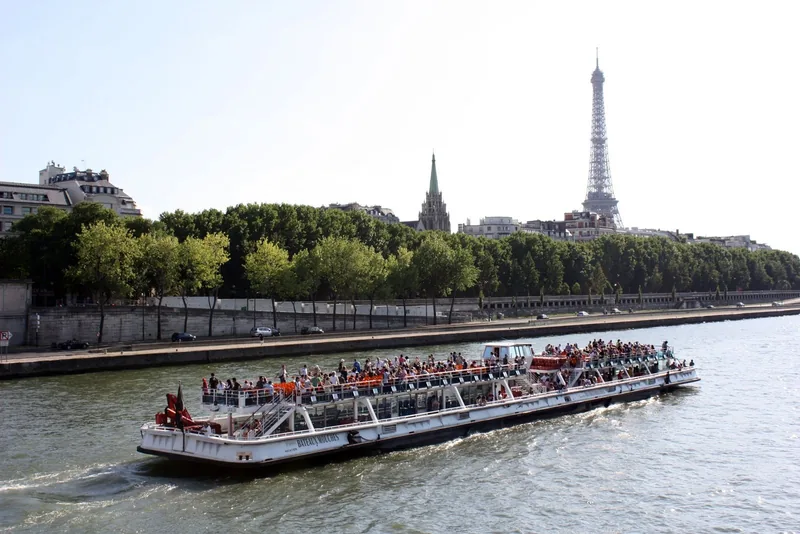 Một tàu du lịch đông khách lướt trên sông Seine với tháp Eiffel vươn cao phía sau ở Paris.