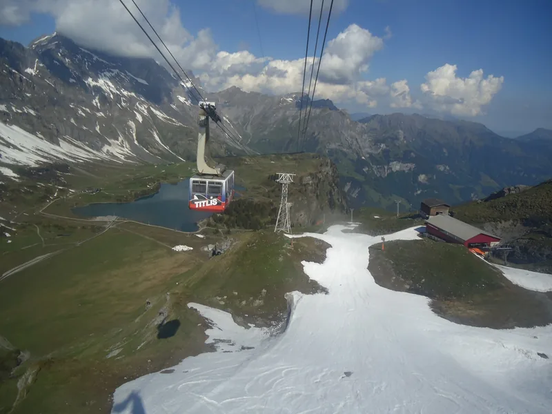 Cáp treo xoay Titlis lướt qua hồ nước trên núi và sườn dốc phủ tuyết tại núi Titlis.